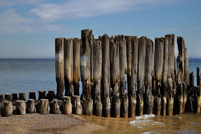 Wooden posts in sea against sky