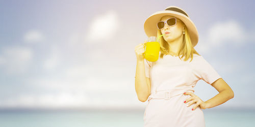Woman wearing sunglasses standing by sea against sky