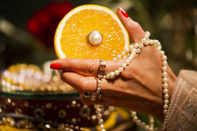 Cropped hand of woman wearing jewelry holding orange