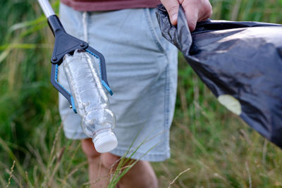 Man volunteer picking up a discarded plastic bottle into a black trash bag from grass.