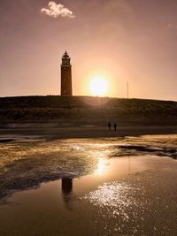 Silhouette lighthouse by sea against sky during sunset