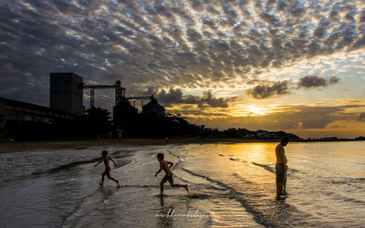 People playing on beach against sky during sunset