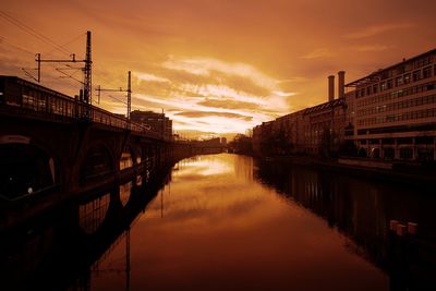 Bridge over river in city against sunset sky