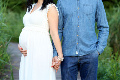 Man holding hands of pregnant woman while standing at park