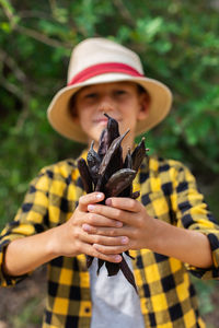 Young boy holding in hands ripe brown carob pods during harvesting season in countryside