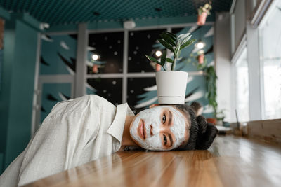 Portrait of woman with face mask lying on table at home