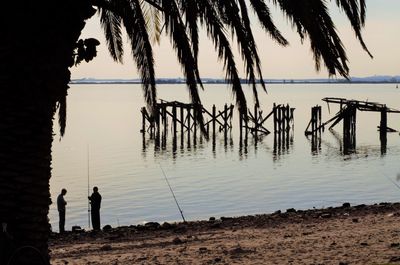 Silhouette fishermen standing at beach against sky during sunset