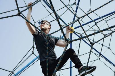 Low angle view of mid adult man climbing rope against clear sky