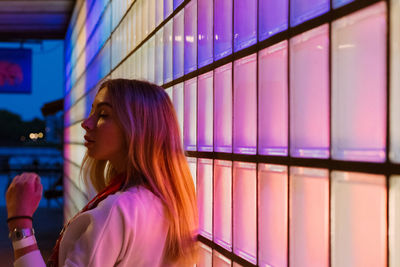 Young woman by illuminated wall