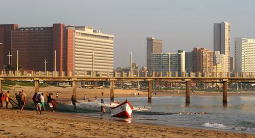 Fishermen at beach by buildings against clear sky