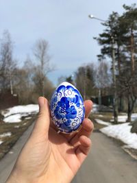 Cropped hand of person holding painted egg against blue sky