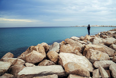 Man standing on rock by sea against sky