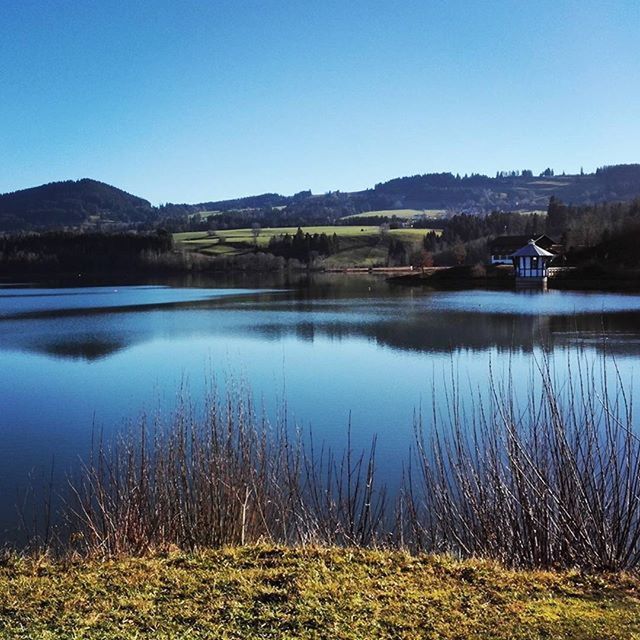 water, clear sky, lake, reflection, tranquil scene, tranquility, blue, scenics, copy space, beauty in nature, mountain, nature, grass, countryside, standing water, calm, idyllic, lakeshore, river, landscape