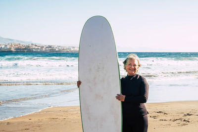 Portrait of senior woman holding surfboard at beach