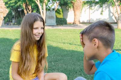 Two teenage friends, a boy and a girl, communicate in a summer green park on a sunny day. 