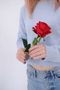 Cropped hand of woman holding flower against white background