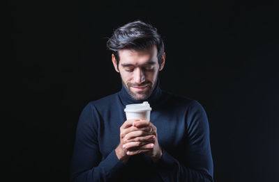 Close-up of young man drinking milk against black background