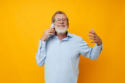 Portrait of senior man talking on phone against yellow background