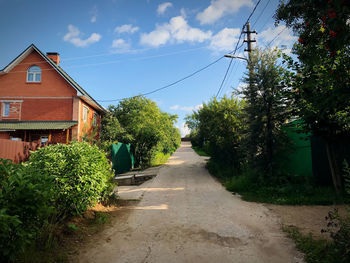 Road amidst trees and buildings against sky