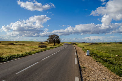 Empty road amidst field against sky