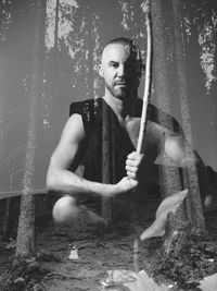 Portrait of young man holding tree trunk