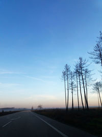 Road by trees against sky during sunset