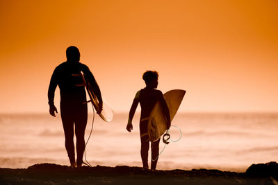 Silhouette people on beach against sky during sunset