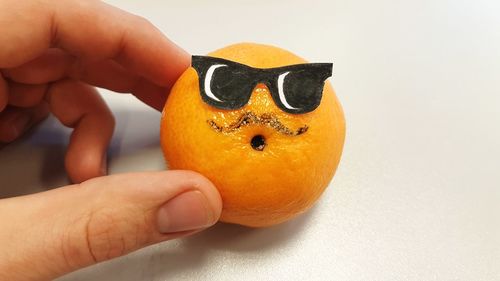 Cropped hand of person holding anthropomorphic face on orange fruit over table