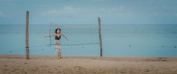Woman jumping at beach seen through volleyball net