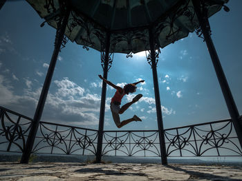 Low angle view of woman jumping in gazebo against sky