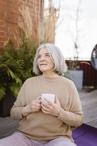 Thoughtful senior woman with cup while sitting at terrace