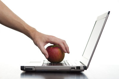 Cropped image of man keeping apple on laptop against white background