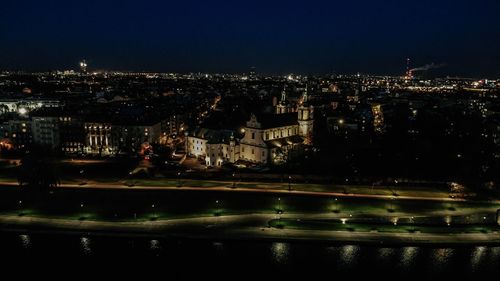 Illuminated buildings by river against sky at night