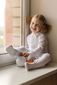 Full length of girl with stuffed toy sitting by window