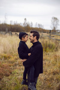 Father and son are standing on a field in autumn in black clothes