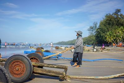 Full length of man holding cart while standing on shore at beach against sky