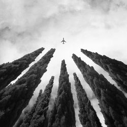 Low angle view of airplane flying over mountains against sky