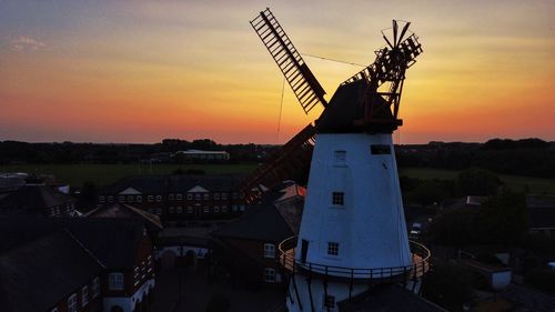Traditional windmill by building against sky during sunset