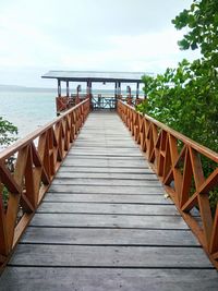 Empty long wooden jetty leading to sea against sky