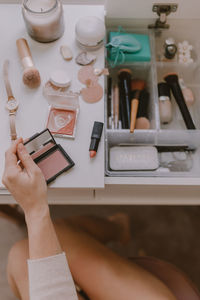 Cropped hands of woman holding beauty products on table at home