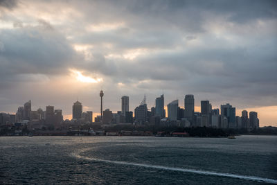 Sea by buildings in city against sky during sunset