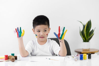 Portrait of boy holding multi colored pencils on table