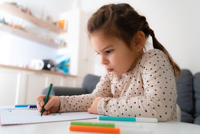 Portrait of cute preschooler child girl drawing with pencils at home while sitting in front