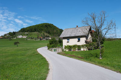 Road amidst field and houses against sky