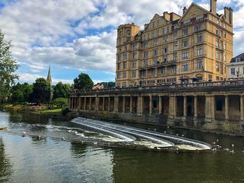 Arch bridge over river by buildings against sky