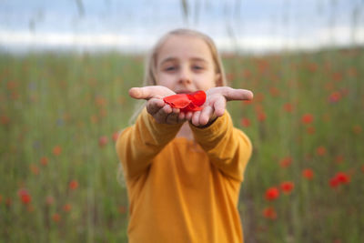 Portrait of cute girl holding red flower on field