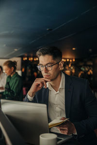 Businessman with hand on chin looking at laptop while sitting in hotel