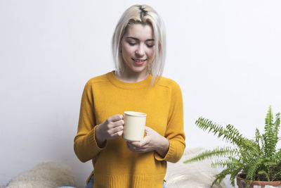 Portrait of young woman holding coffee cup while standing against white background