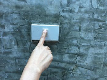 Close-up of cropped hand pressing light switch on wall