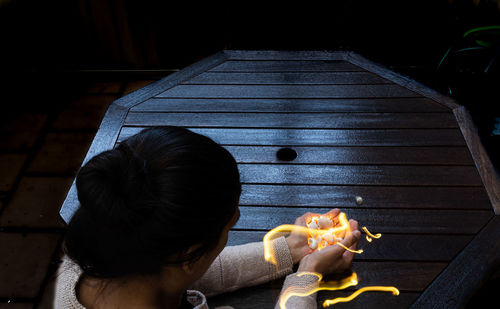 Rear view of woman holding food while sitting on wood